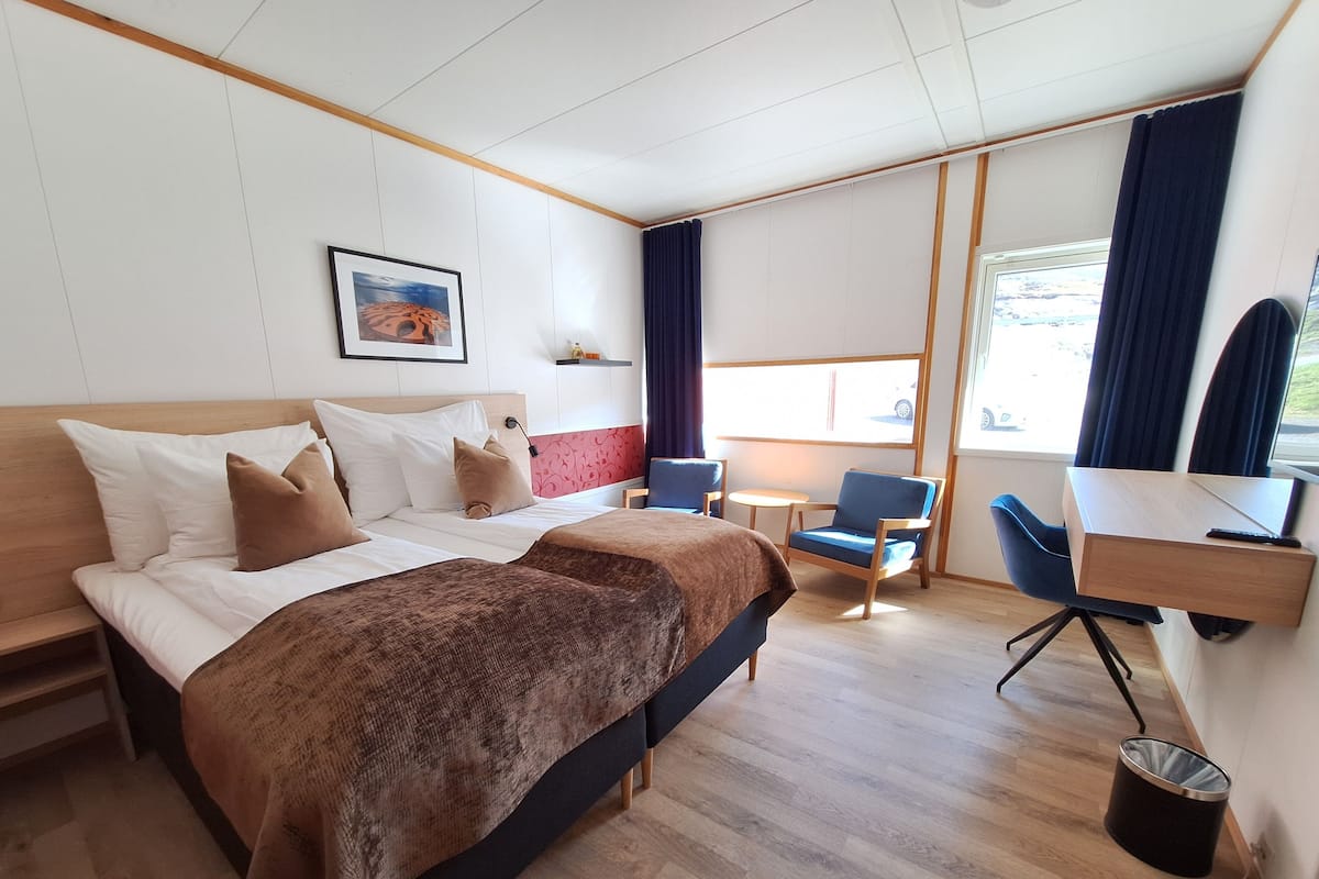 Een hotelkamer met een bed, twee stoelen, een bureau en een raam met gordijnen.