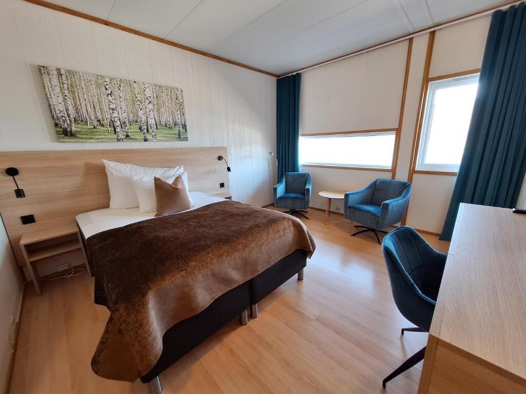 Une chambre d’hôtel avec un lit, un bureau, deux chaises, une petite table et un tableau au mur.