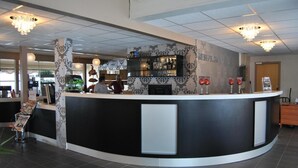 A modern reception area with a curved counter, decorative wall panels, and a bar area with glassware. - Tjeldsundbrua Hotel (Tjeldsund)