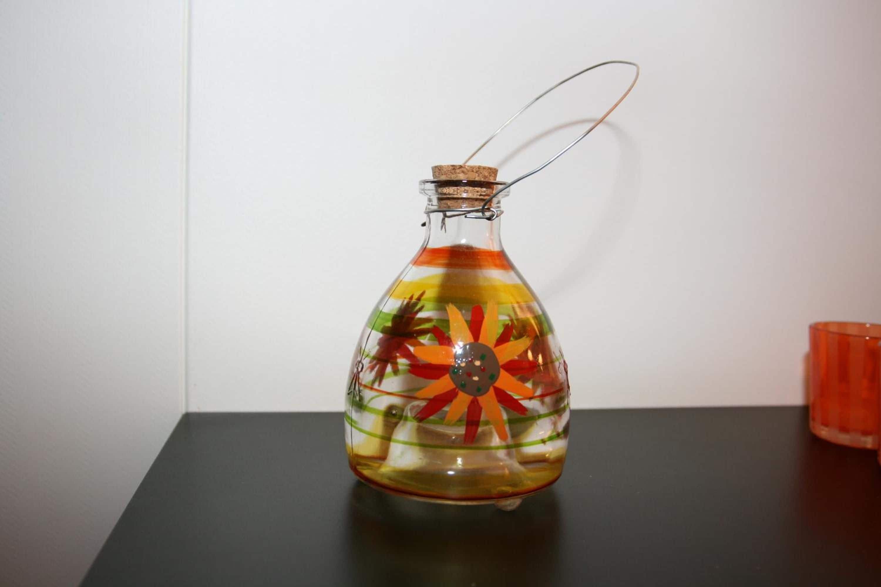 Una botella de vidrio con tapón de corcho y un lazo de alambre metálico, que contiene un líquido colorido con un diseño floral.