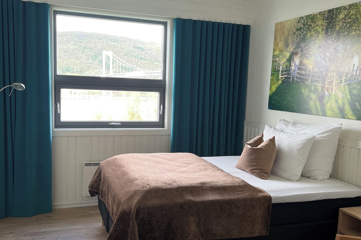 Een slaapkamer met een bed, een raam met gordijnen, een schilderij aan de muur en een houten vloer.