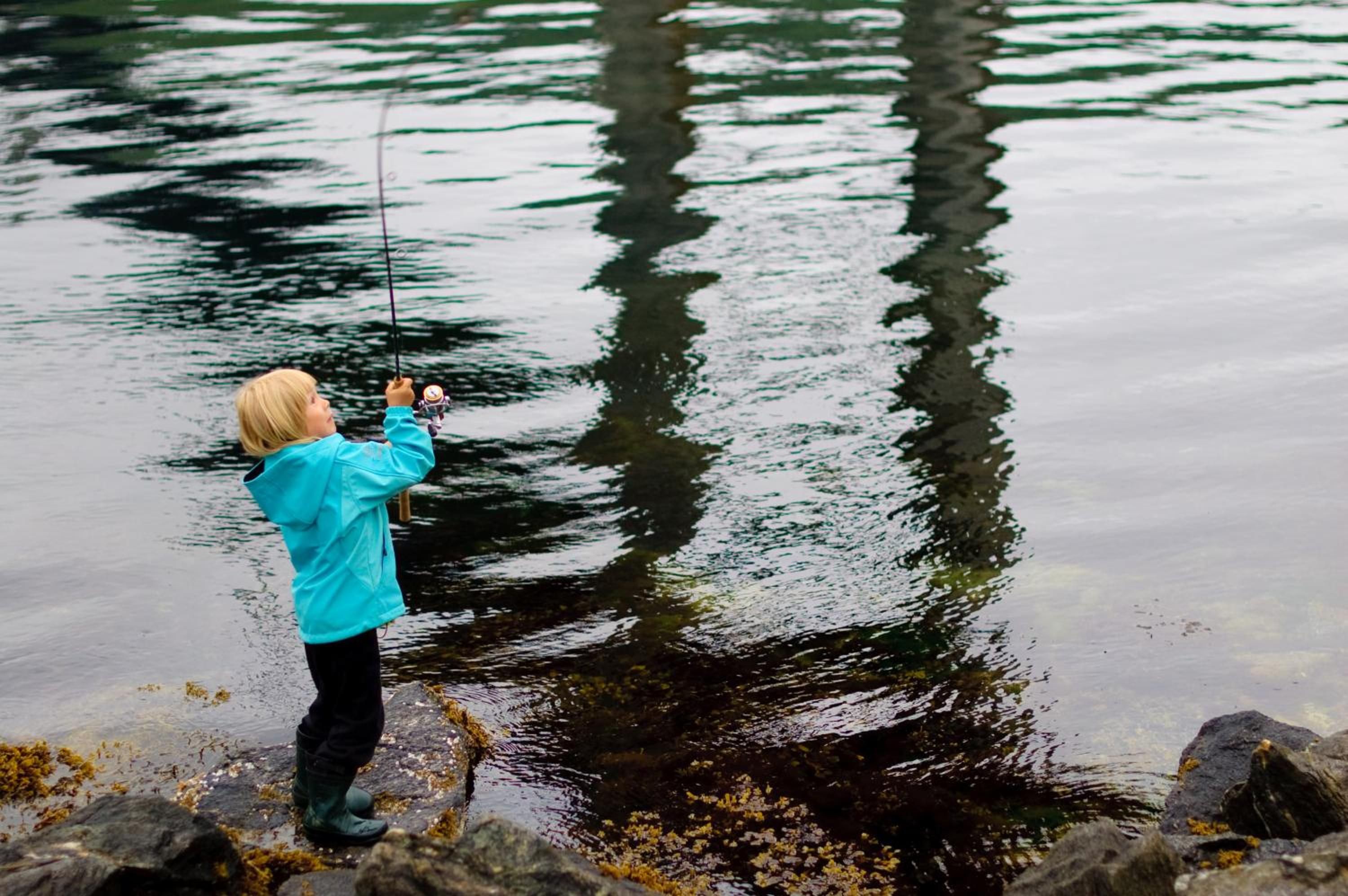 A person fishing by a calm body of water with reflections of trees.
