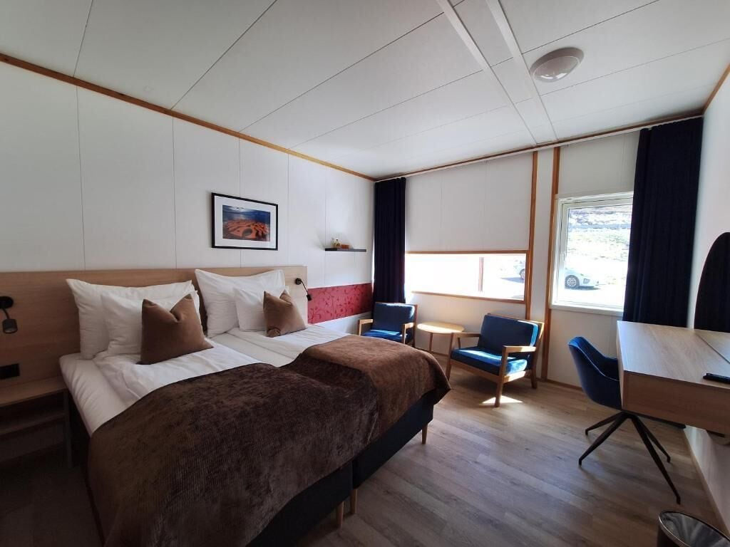 A hotel room with two beds, a desk, a chair, a small table, and a window.