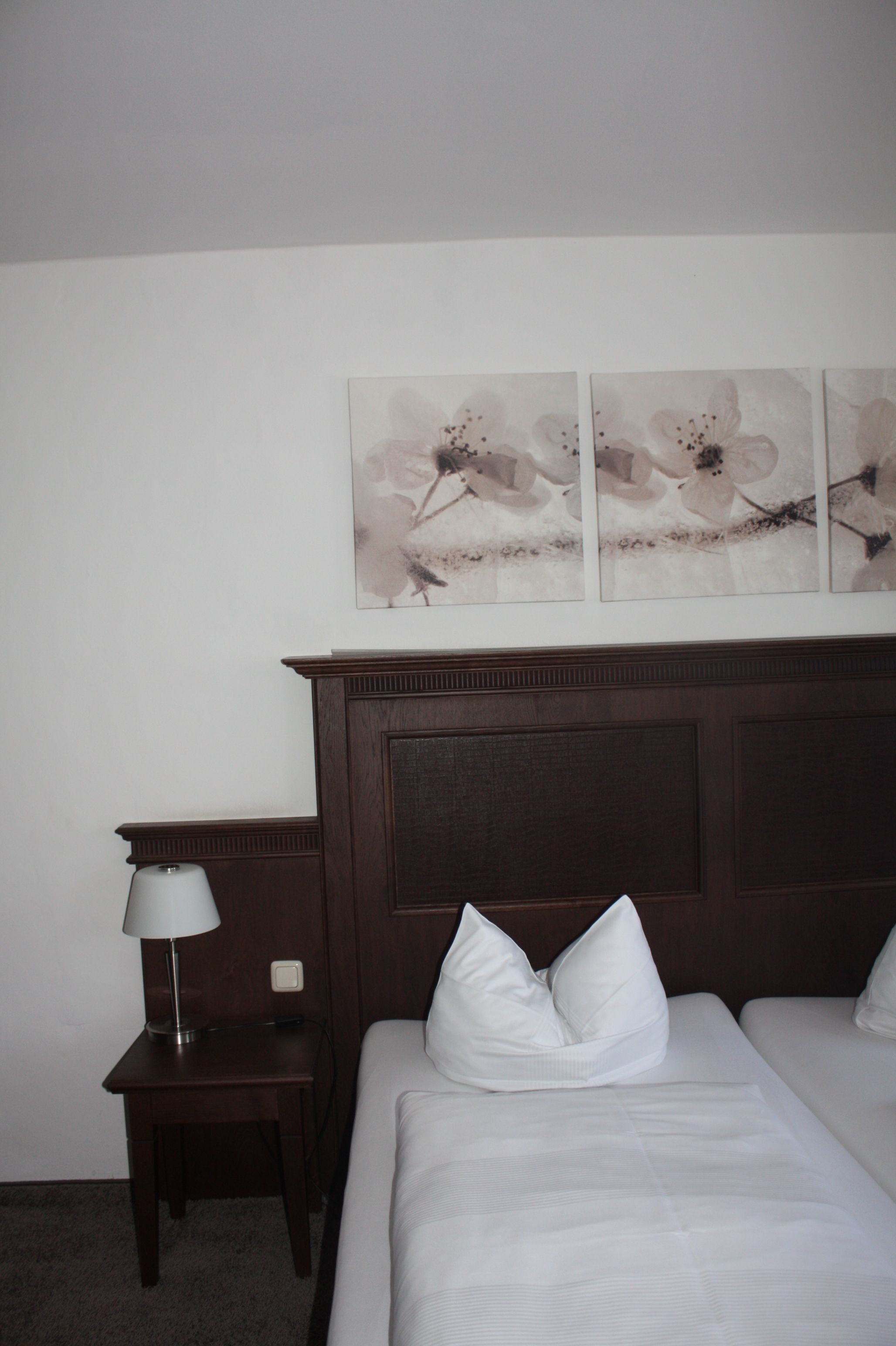 A hotel room with a bed, a nightstand with a lamp, and a wall-mounted artwork.