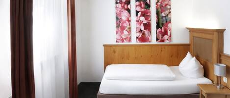 Een hotelkamer met een houten hoofdbord, een bed met witte lakens, een klein nachtkastje met een lamp en een groot bloemenkunstwerk aan de muur.