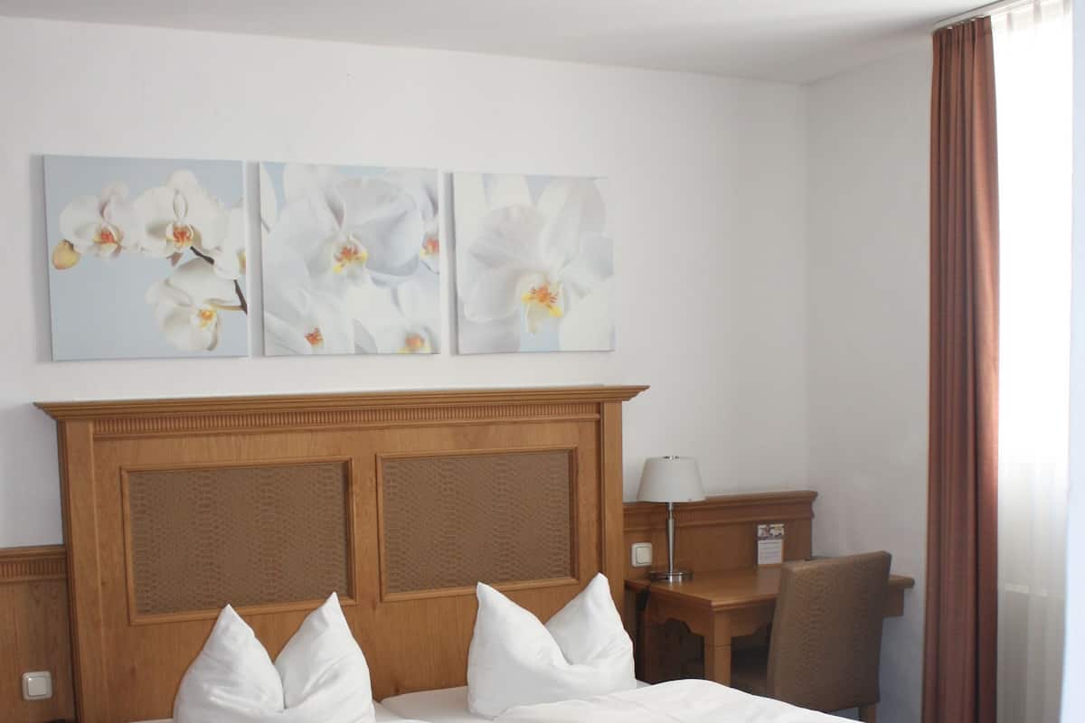 A hotel room with a double bed, a wooden headboard, a desk, a chair, and artwork on the wall.
