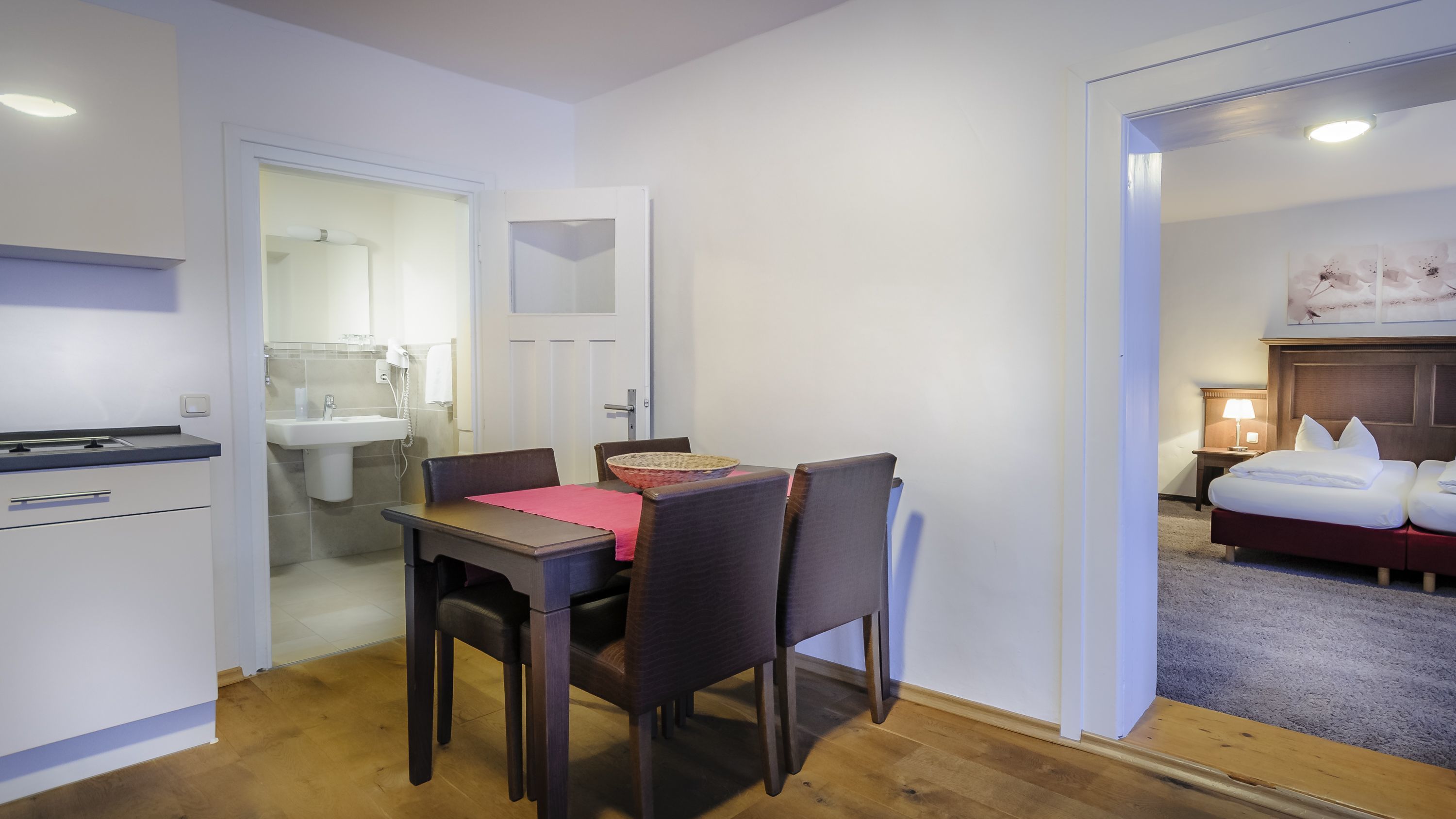 A compact hotel room with a dining area, a small kitchenette, a bathroom, and a bed.