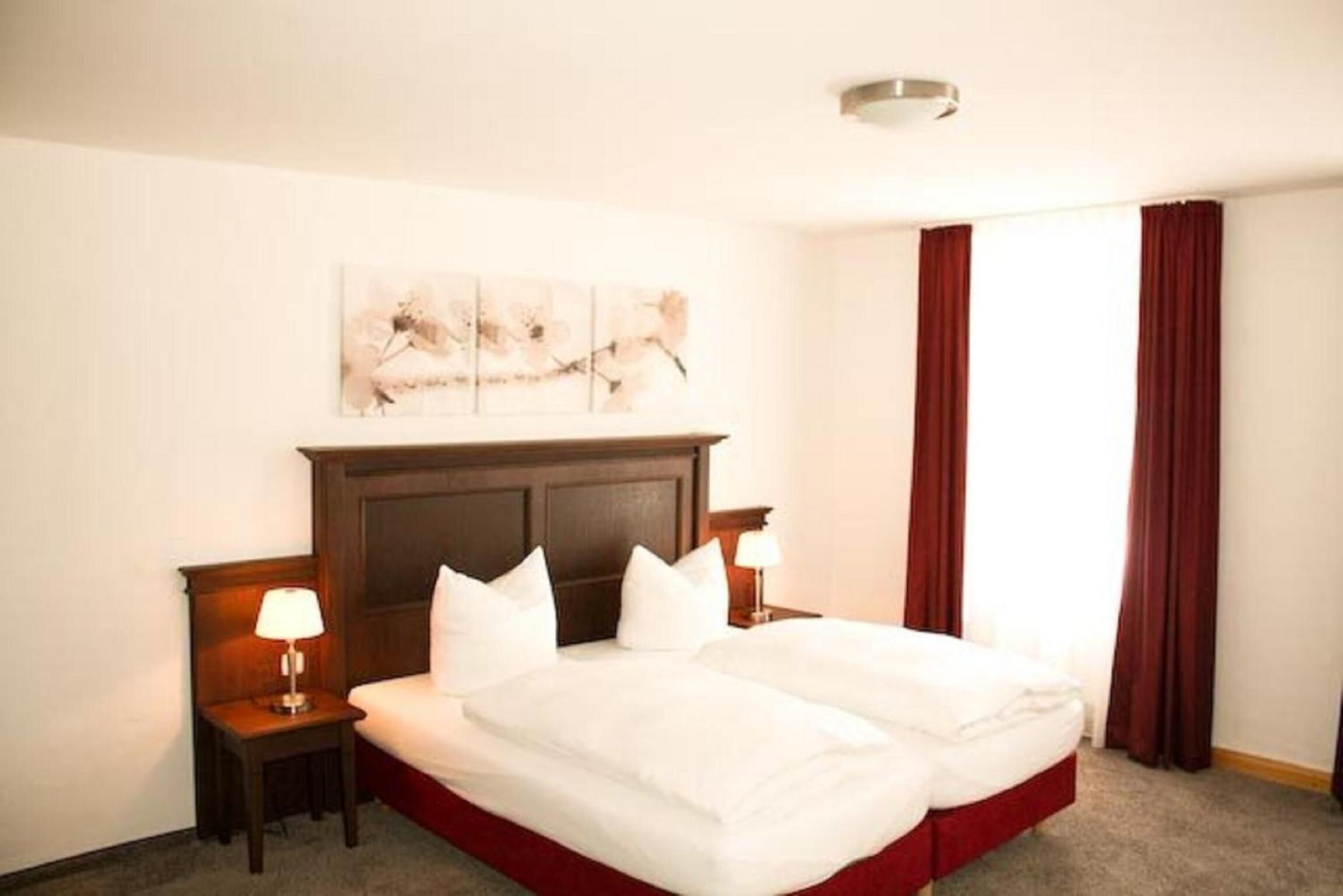 Un cuarto de hotel con una cama grande, dos mesitas de noche con lámparas, un cabecero y un cuadro en la pared.