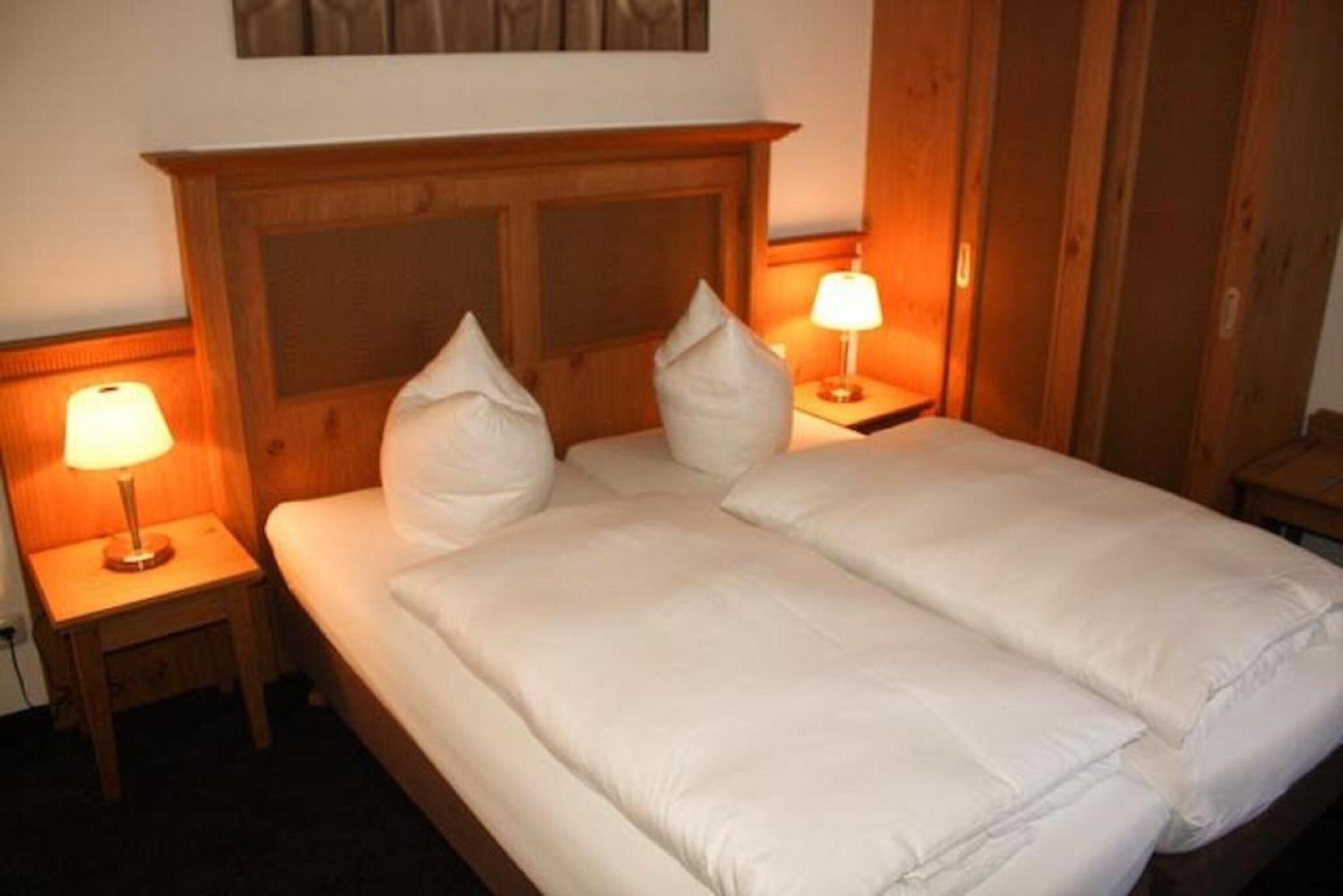 A double bed with white bedding, two bedside lamps, and a wooden headboard.