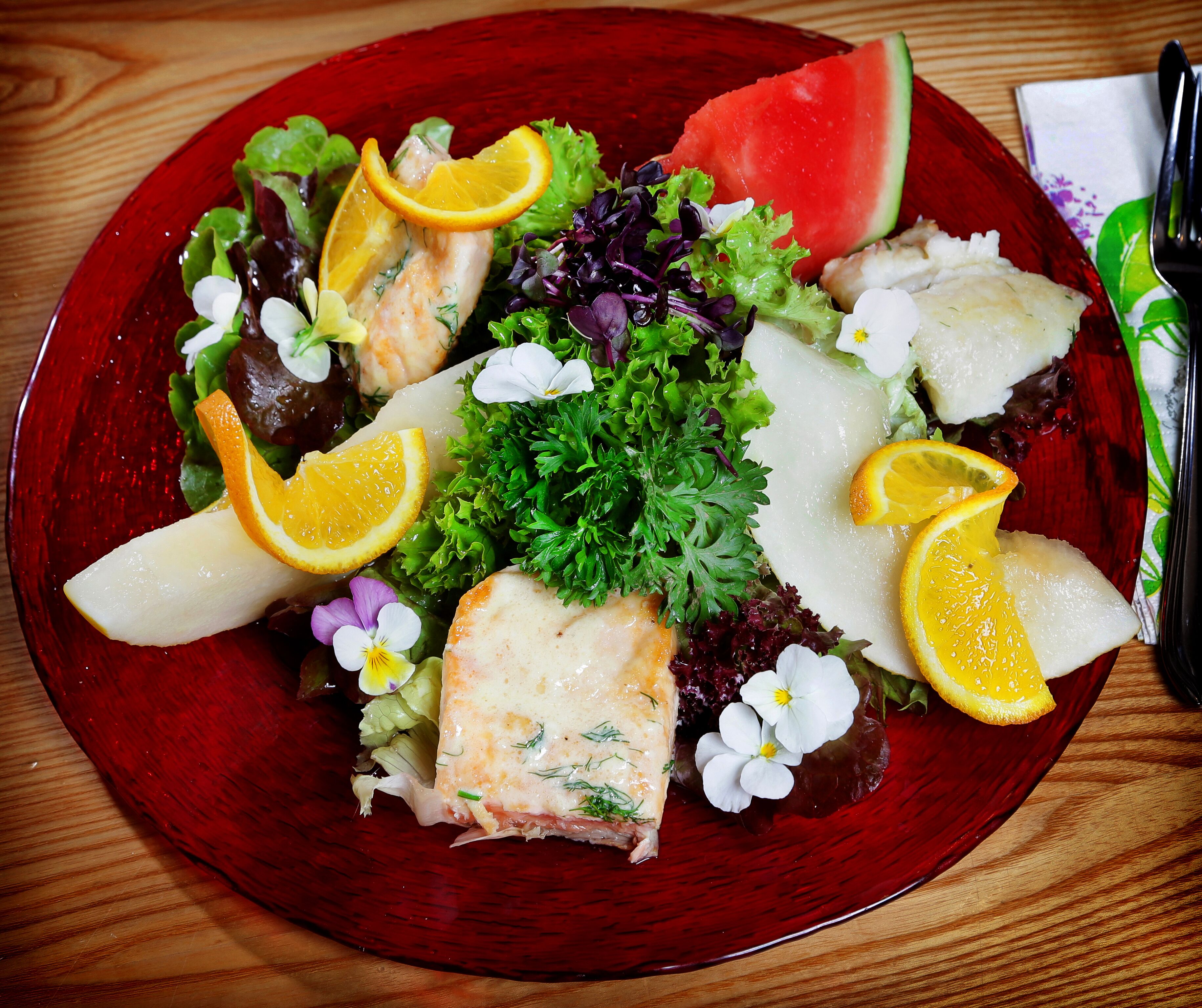 Ein Teller mit Salat, darunter Blattsalat, Fisch und Orangenscheiben.