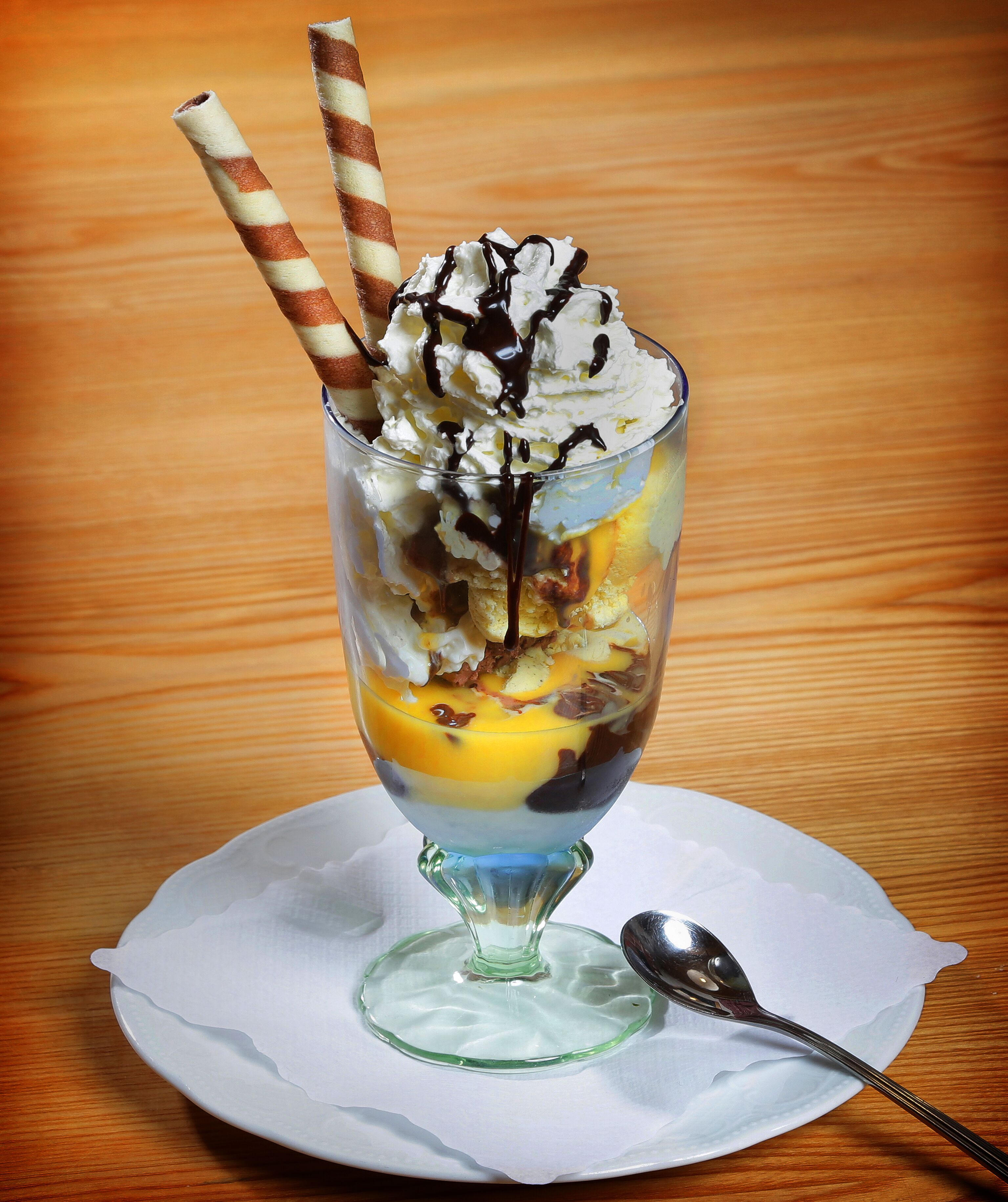 Un dessert servi dans un verre, accompagné d’une cuillère posée sur une assiette blanche.