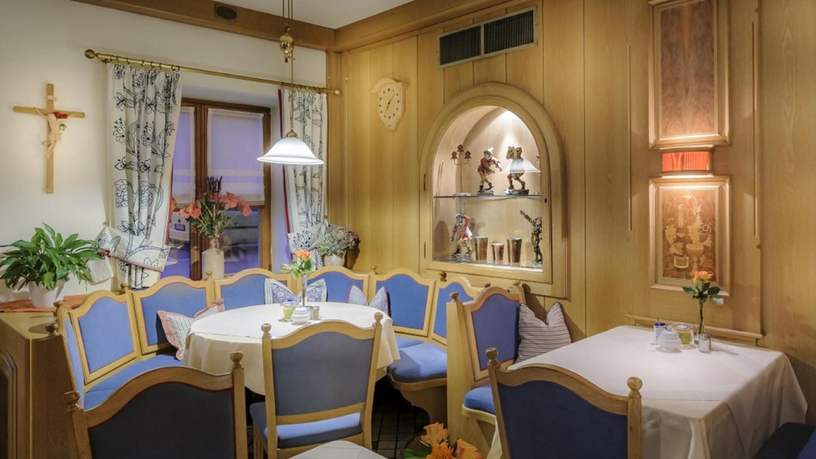 A dining area with a wooden interior, blue upholstered chairs, a round table, and a cross on the wall.