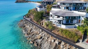 A coastal property with a pier extending into the sea, modern houses with large windows, and a clear view of the ocean and distant hills. - Ocean Azul – Modern Infinity-Pool Villa Overlooking Darkwood Beach, Antigua and Barbuda (Ffryes beach)