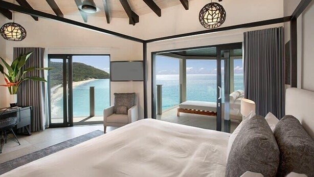 A modern hotel room with a large bed, a desk, and a view of the sea. - Ocean Azul – Modern Infinity-Pool Villa Overlooking Darkwood Beach, Antigua and Barbuda (Ffryes beach)