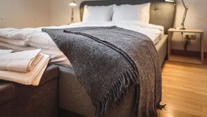 Un letto rifatto con cura, con una coperta grigia, cuscini bianchi e una lampada da comodino su un tavolino di legno.