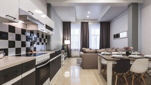 Una cucina moderna con zoccolo a scacchi bianchi e neri, un'area pranzo con tavolo imbandito per quattro persone e un soggiorno con divano e televisore.