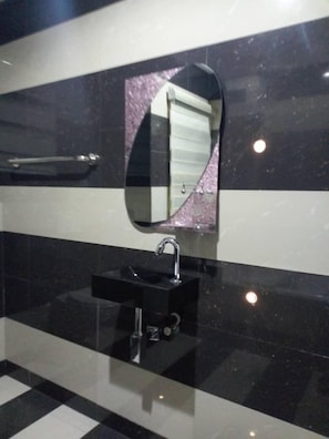 A bathroom with a black and white checkered floor, a black sink with a chrome faucet, and a mirror with a pink frame. - Cadestral Zone Hotel (Abuja)