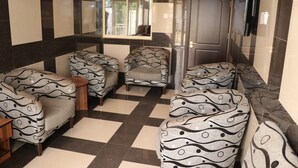 Un hall d'entrée avec des canapés à motifs, un sol à carreaux, un miroir et une porte sur laquelle est apposée une pancarte « Il est interdit de fumer ».