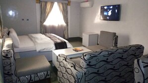 Une chambre d’hôtel avec un lit, une télévision, un bureau et deux fauteuils à motifs.