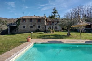 Una casa de piedra con piscina, jardín y pérgola.