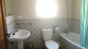 Uma casa de banho com lavatório, sanita, banheira e uma janela.