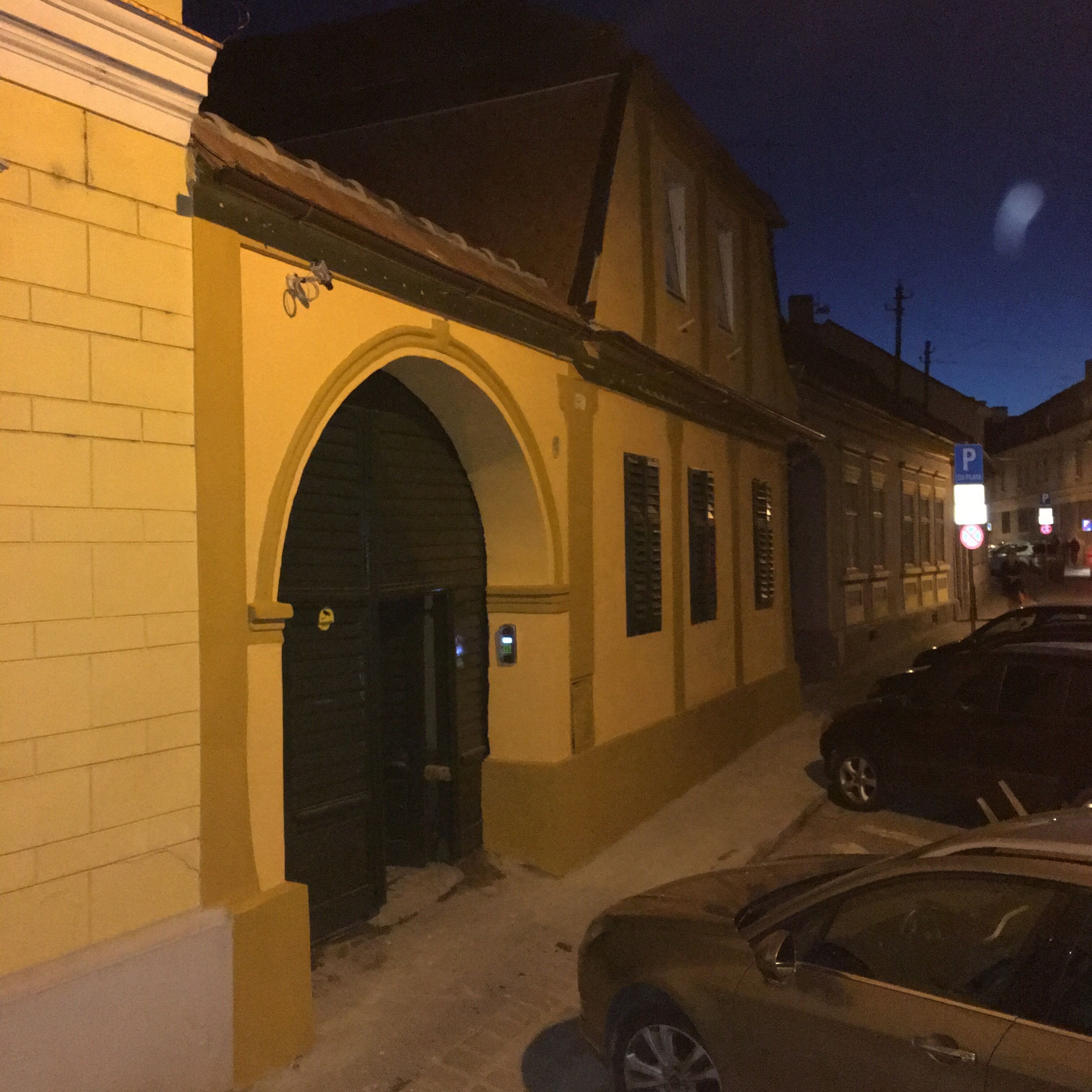 A building with a yellow facade, a black archway entrance, and a parked car in front.