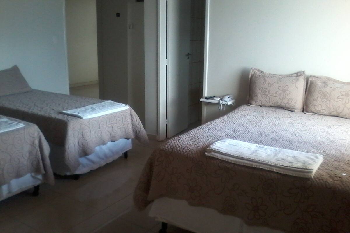 A hotel room with two single beds, a bedside table with a phone, and a door leading to another room.