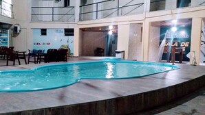 A swimming pool with a curved design, surrounded by chairs and tables, and a high ceiling with a balcony. - Hotel Aracaju Express (Aracaju)