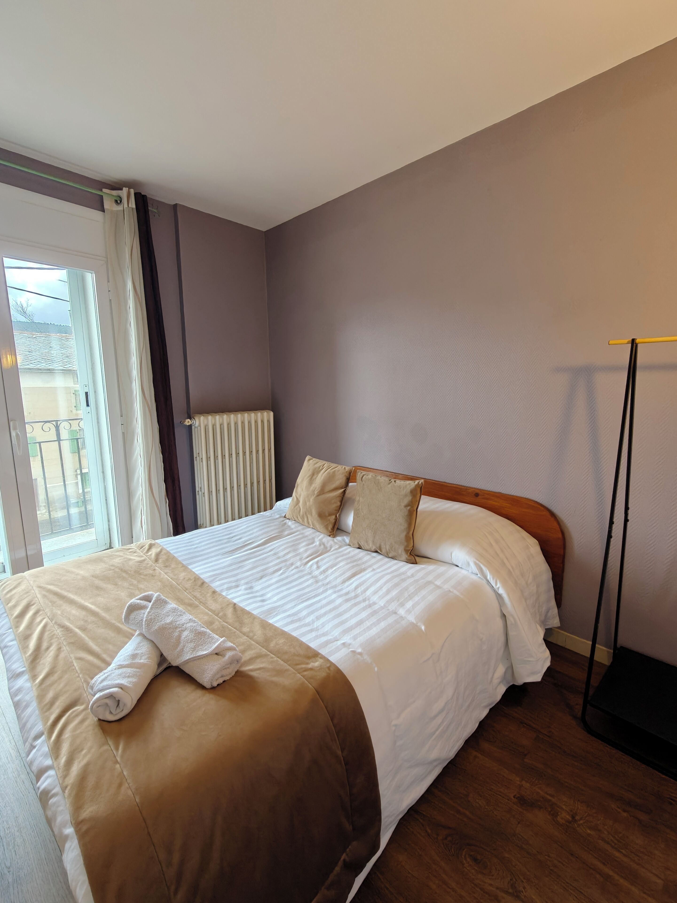 A neatly made bed with a brown and white duvet, a rolled white towel, and two beige pillows.
