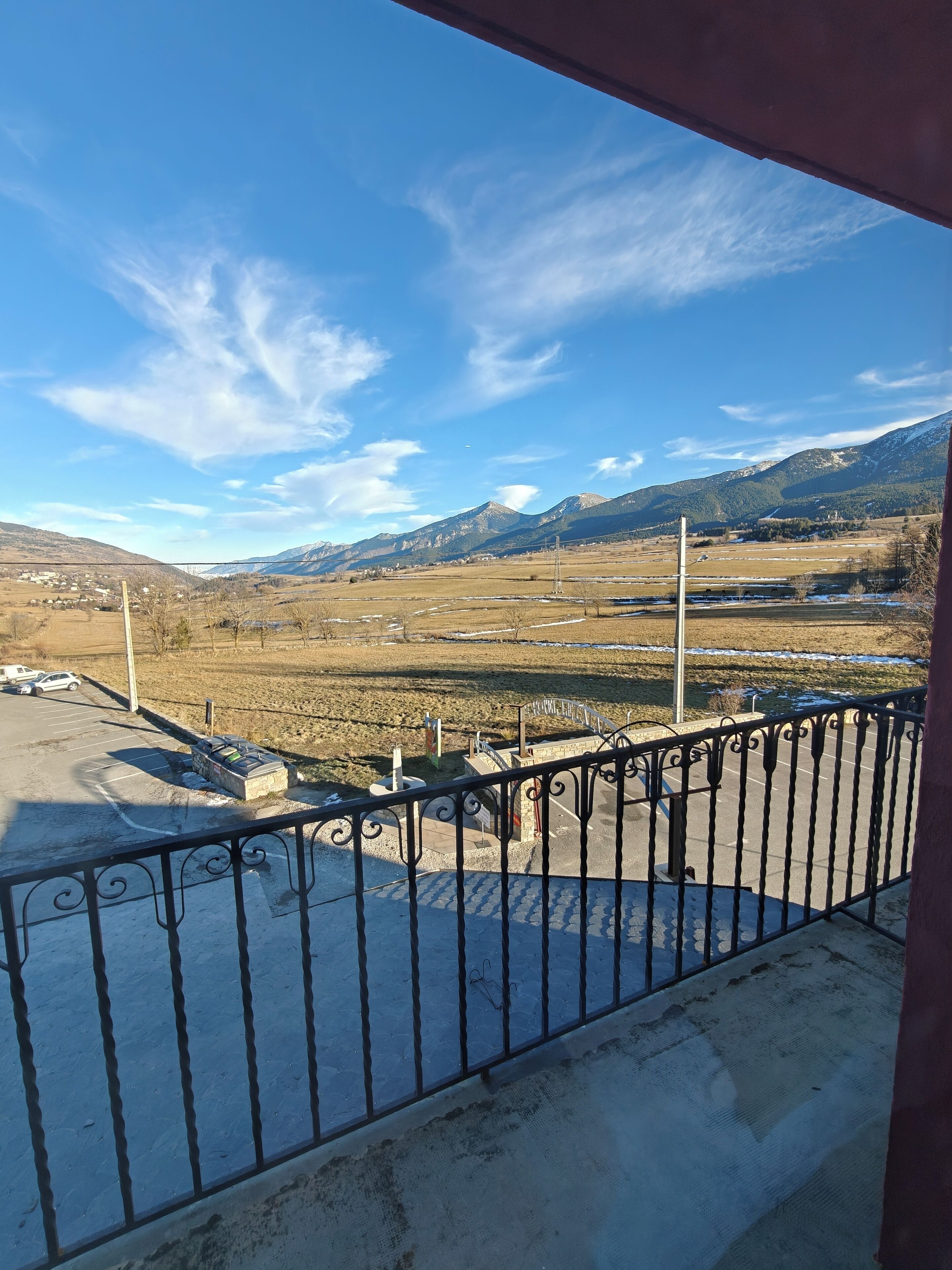 A balcony with a view of a parking lot and distant mountains.