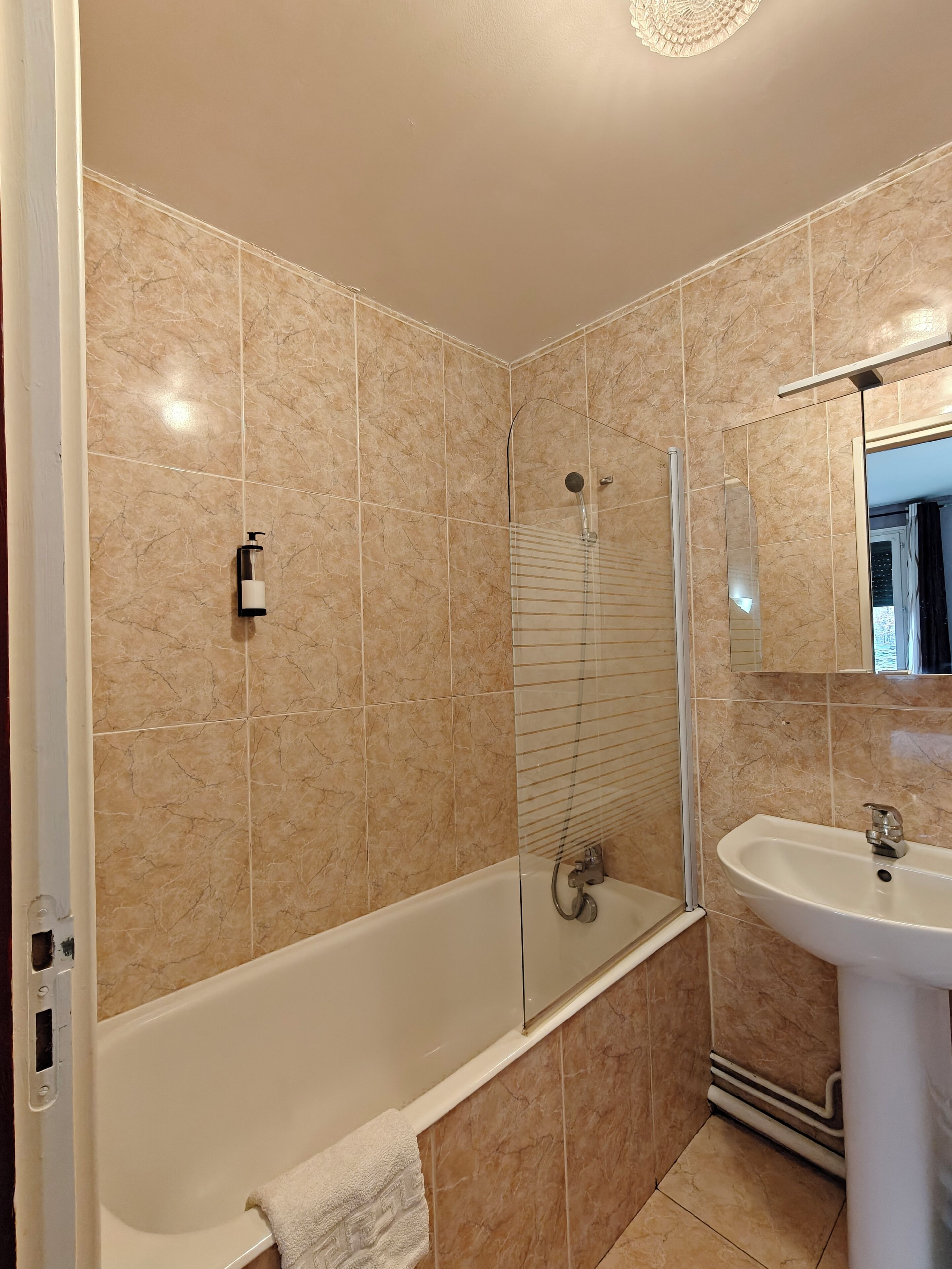 Un baño con bañera, ducha y lavamanos, todo con azulejos de mármol.