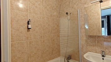 Un baño con bañera, ducha y lavamanos, todo con azulejos de mármol.