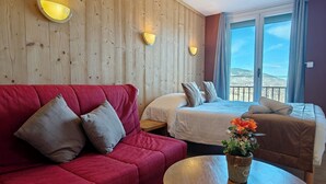 Een hotelkamer met een houten wand, twee bedden, een rode bank, een ronde houten tafel en een potplant.