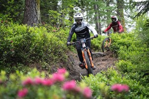Dois ciclistas de montanha numa trilha cercada por vegetação densa e árvores.