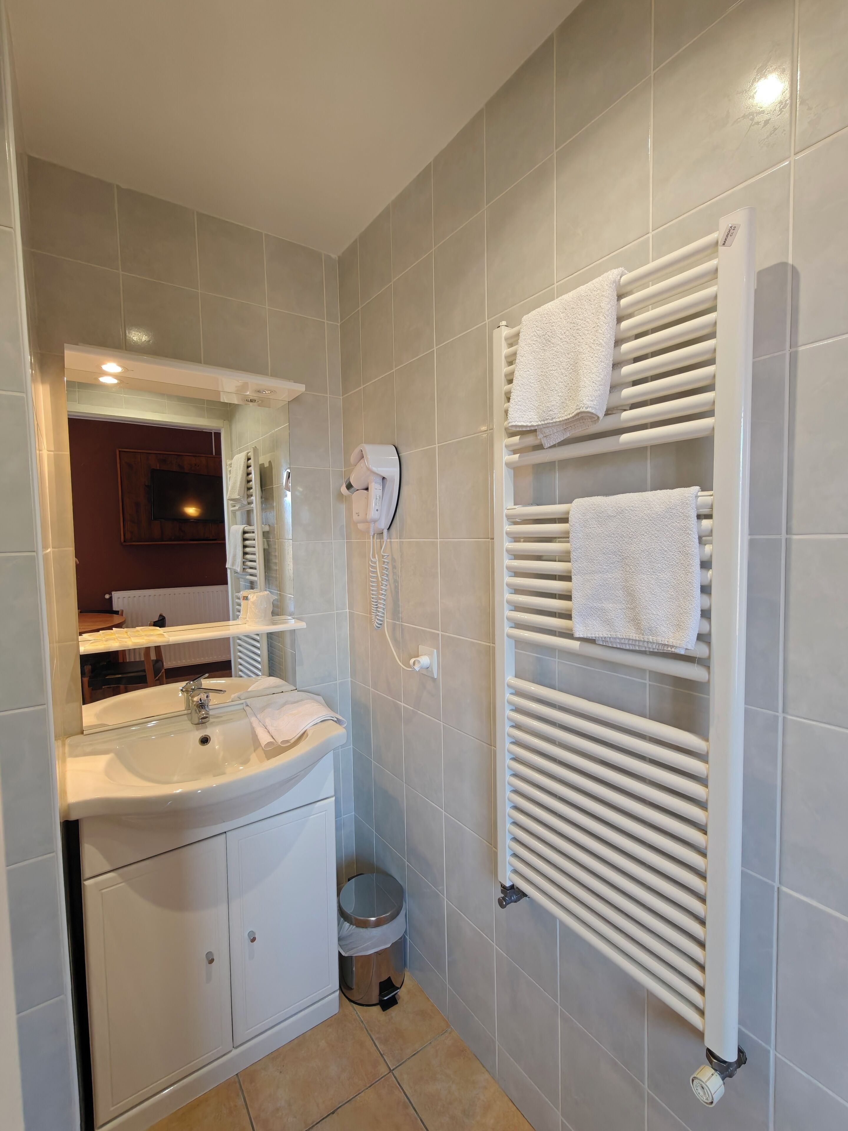 A modern bathroom with a sink, mirror, hairdryer, towel rack, and a radiator.