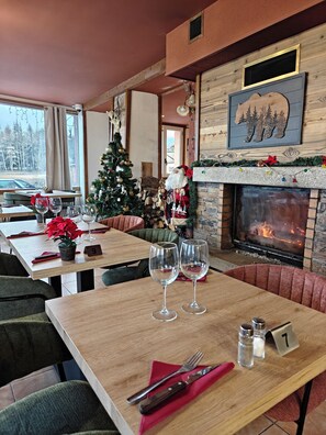 A cozy restaurant with a fireplace, Christmas decorations, and a view of the outside. - Hôtel Le Catalan (La Cabanasse)