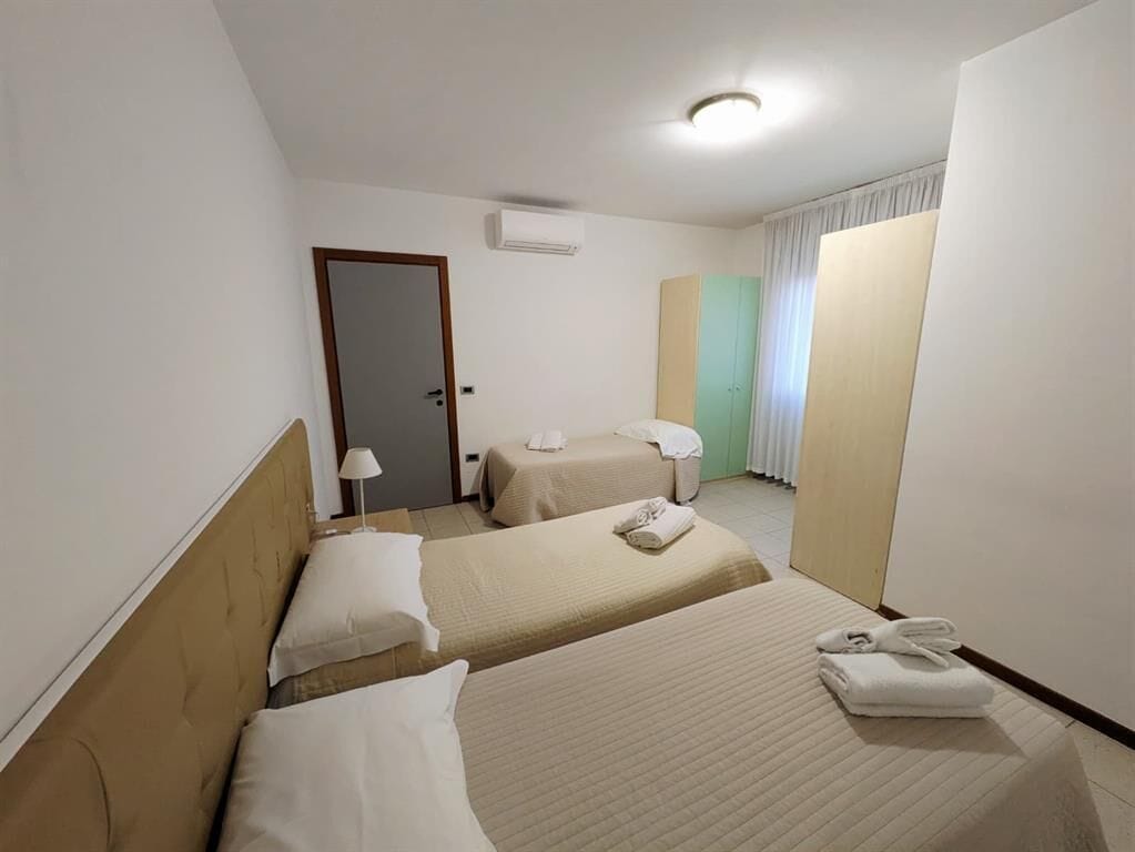 Hotellihuone, jossa on kaksi sänkyä, vaatekaappi, ovi ja ikkuna, jossa on verhot.