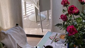 Un comedor con una mesa dispuesta para dos, una silla, un florero y vistas a un jardín.