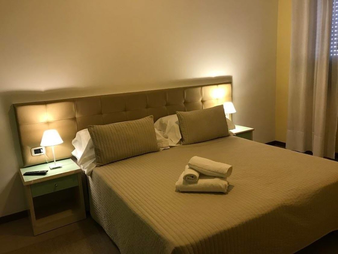 Un lit bien fait, avec une couverture beige et des oreillers, une lampe de chevet et une serviette pliée posée sur la table de chevet.