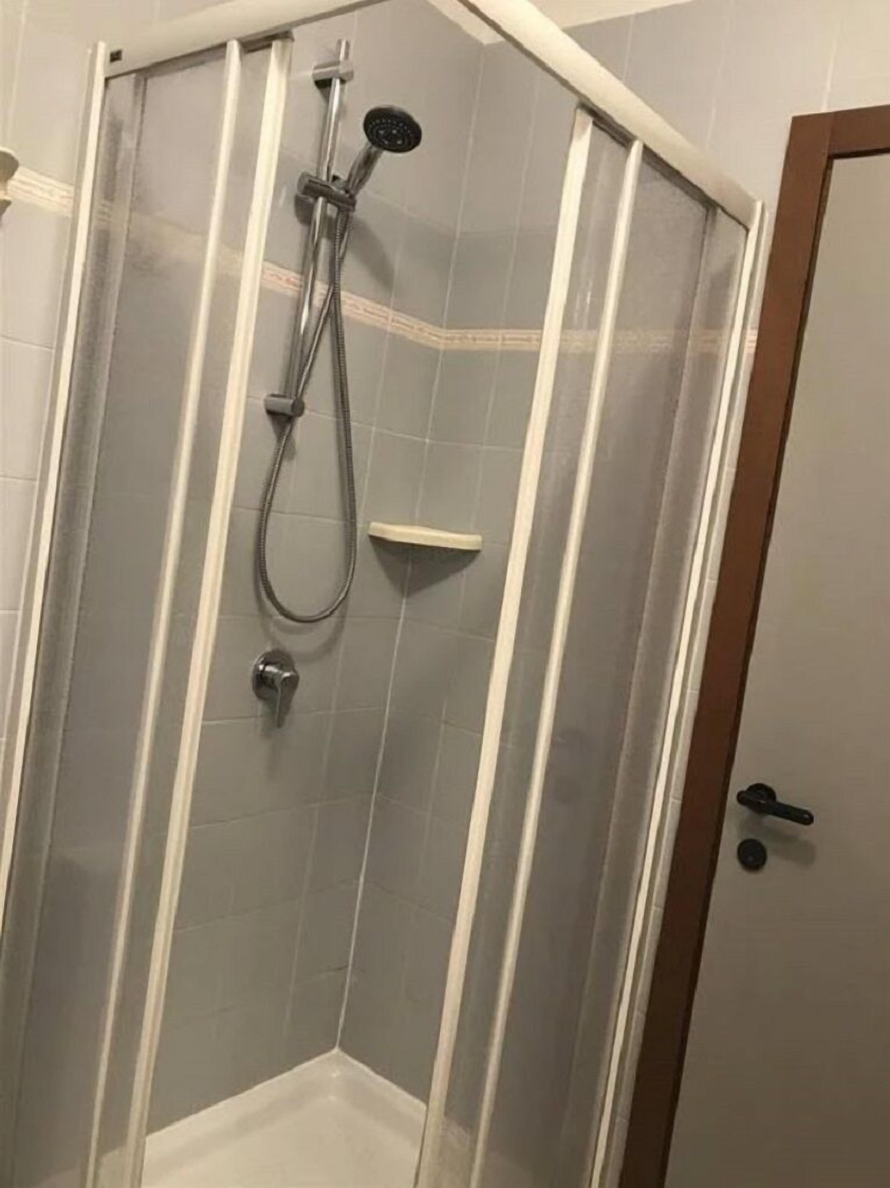 A corner shower enclosure with a glass door, a handheld showerhead, and a wall-mounted control panel.