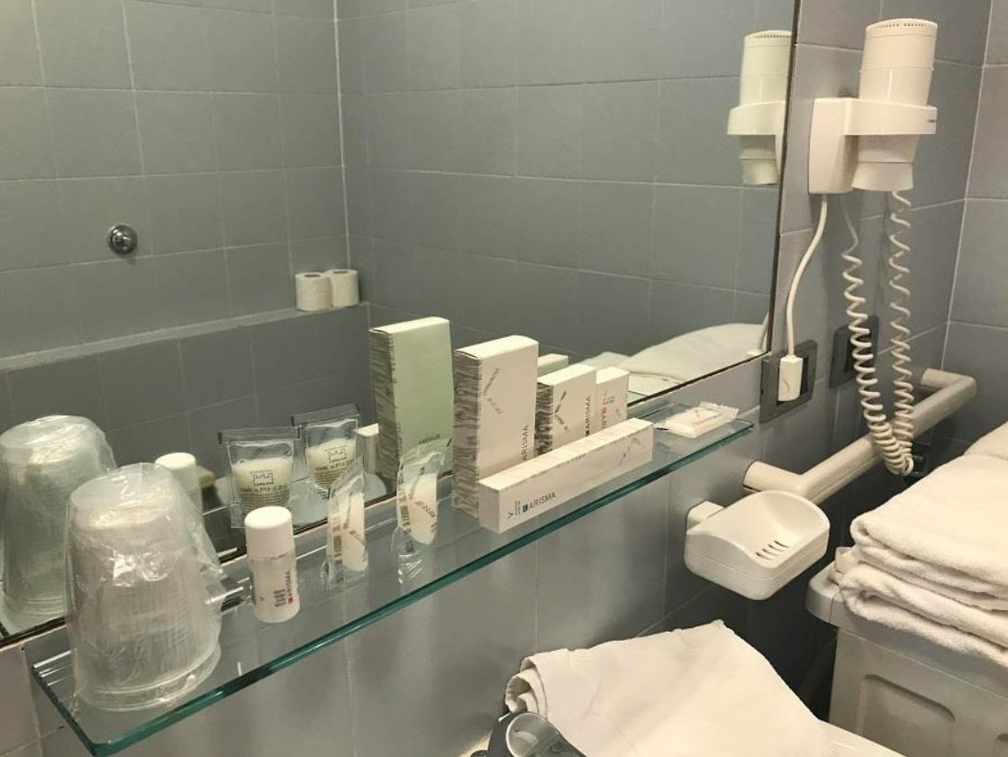 A bathroom with a glass shelf displaying toiletries, a towel rack, and a hairdryer.