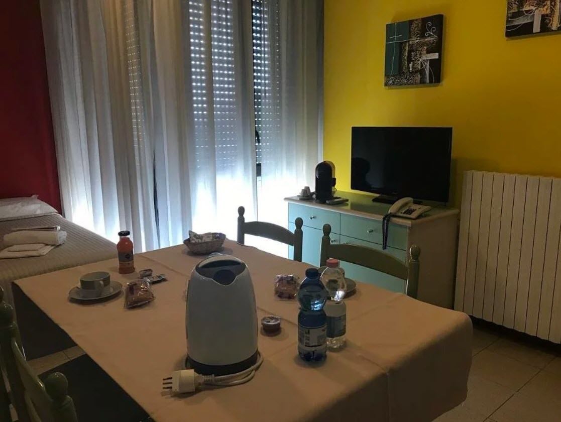 Habitación de hotel con cama, una mesa de comedor con alimentos para el desayuno, hervidor de agua y televisión.