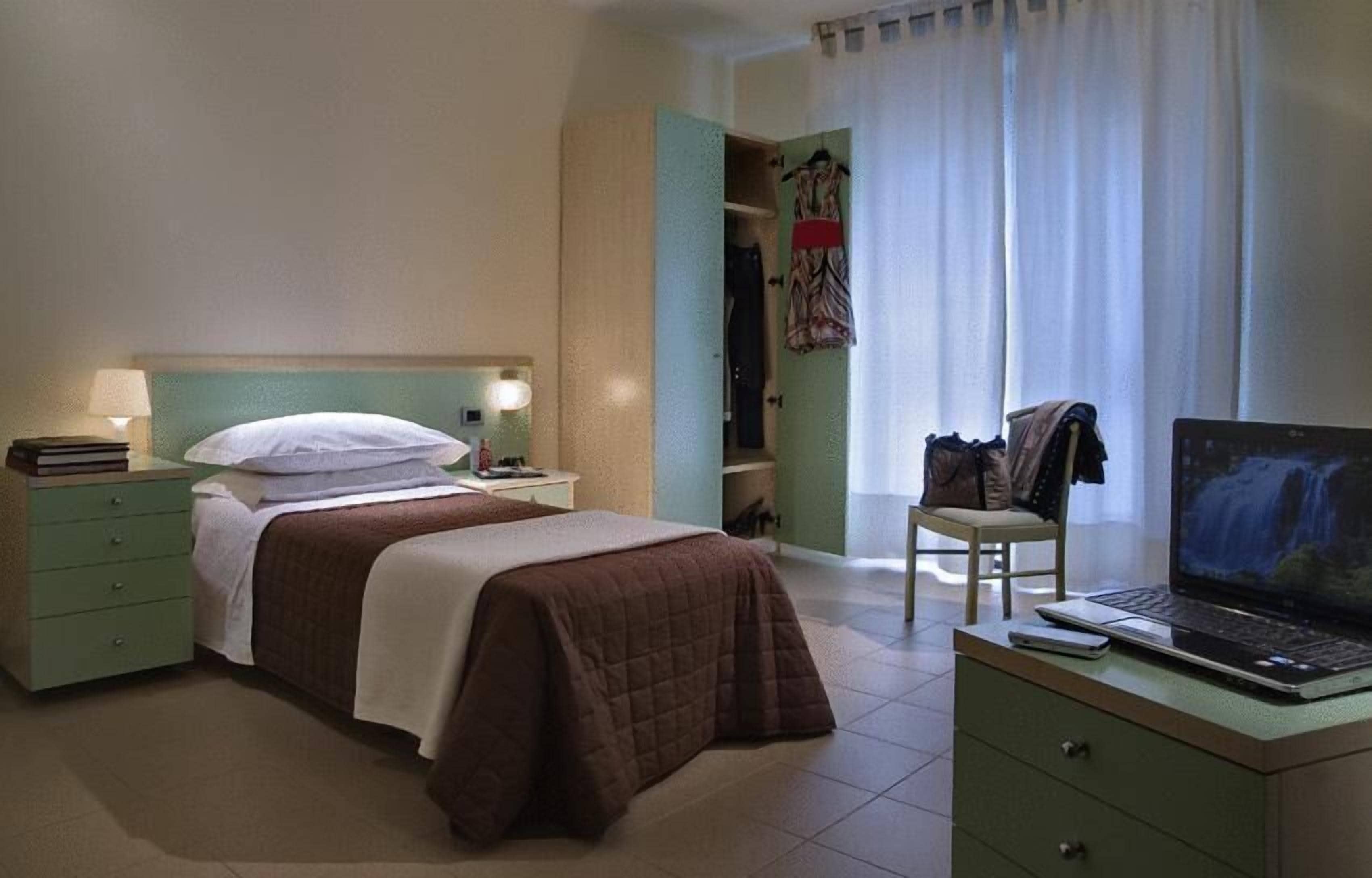 Une chambre d’hôtel comprenant un lit, un bureau avec un ordinateur portable, une chaise et une armoire.