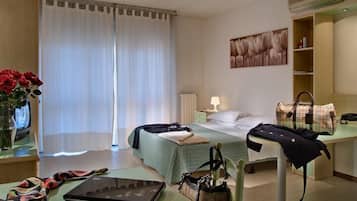 Une chambre d’hôtel avec deux lits, un bureau avec un ordinateur portable, un vase rempli de fleurs rouges, une télévision et un tableau accroché au mur.