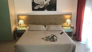 Ein Hotelzimmer mit einem großen Bett, zwei Nachttischen mit Lampen, einem Blumenbild an der Wand und einem Fenster mit roten Vorhängen.