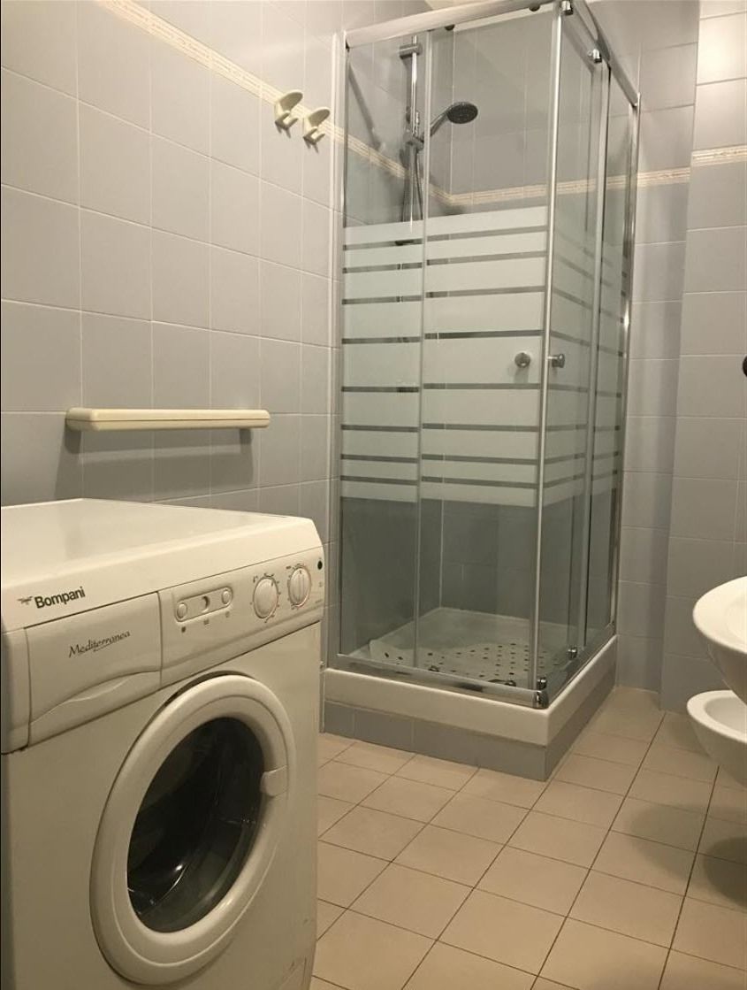 A compact bathroom with a washing machine, a glass-enclosed shower, and a white sink.