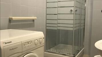 A compact bathroom with a washing machine, a glass-enclosed shower, and a white sink.