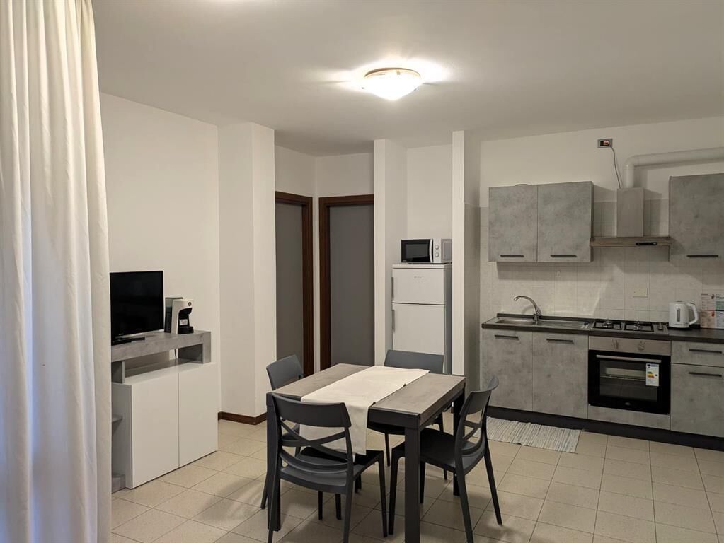 Cocina compacta con microondas, refrigerador y horno. Hay una mesa de comedor con sillas y un televisor sobre un mueble.