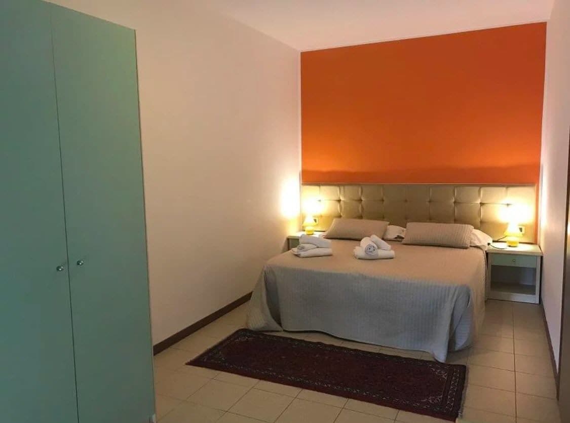 A hotel room with a bed, two bedside tables with lamps, a wardrobe, and a rug.