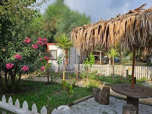 A garden with a thatched structure, a white picket fence, and various plants. - Camping Ulisse (Lamezia Terme)